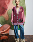 Person wearing Alemais patterned cardigan and blue pants standing in front of a colorful abstract painting.