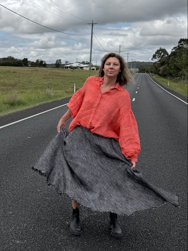 Person standing on a road wearing estilo emporio  with a cloudy sky and fields in the background
