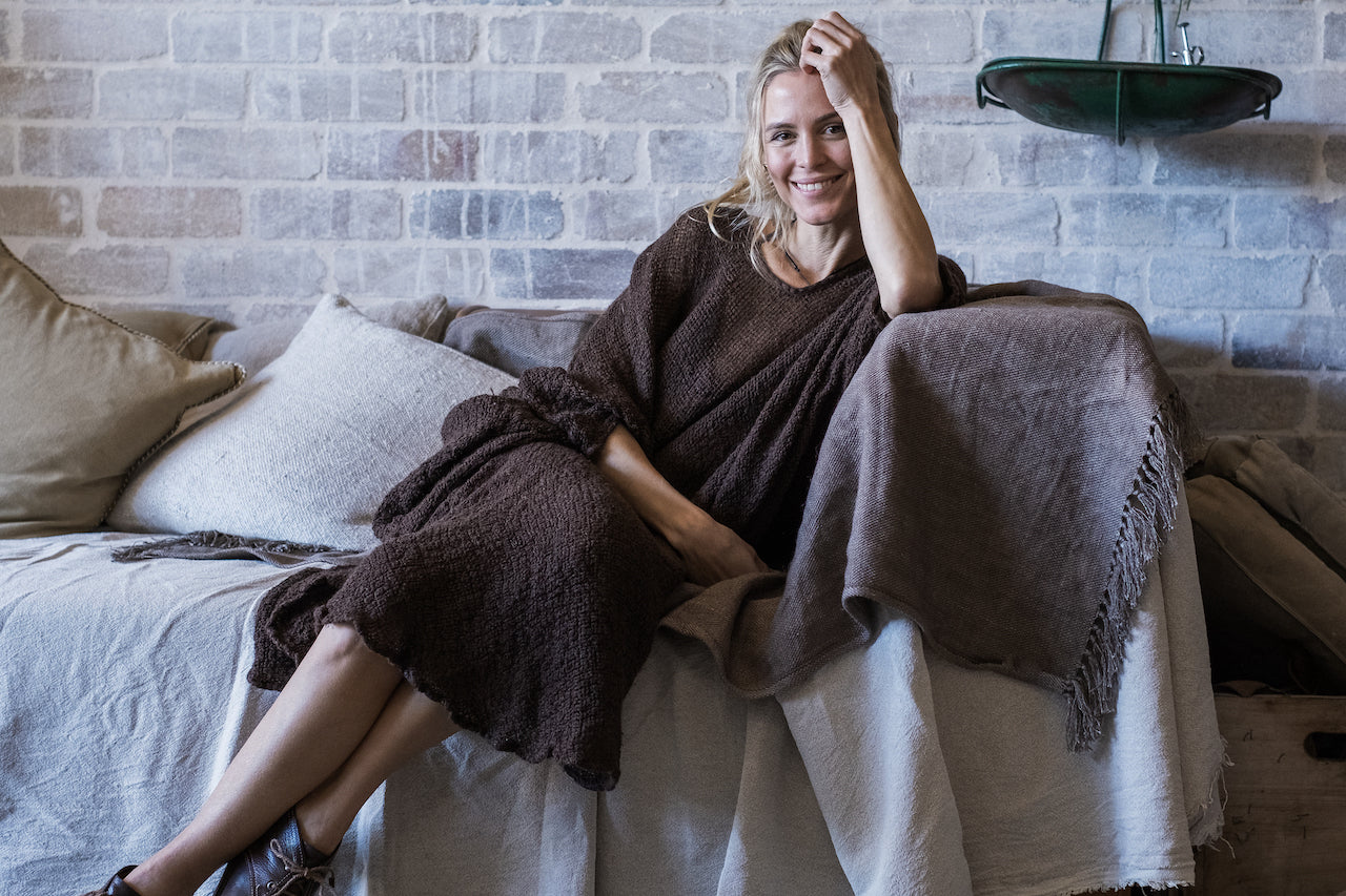 Woman sitting on a couch wearing la bottega di brunella linen dress with a brick wall background