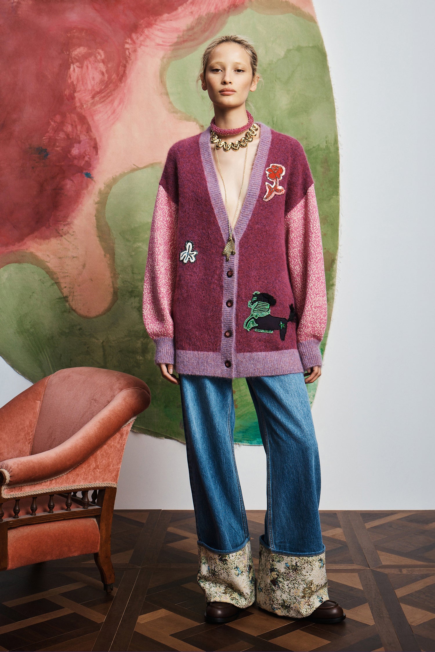 Person wearing Alemais patterned cardigan and blue pants standing in front of a colorful abstract painting.