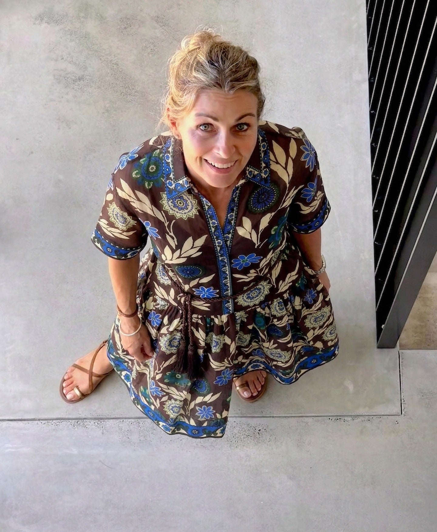 Woman wearing a patterned dress sitting on a concrete floor.