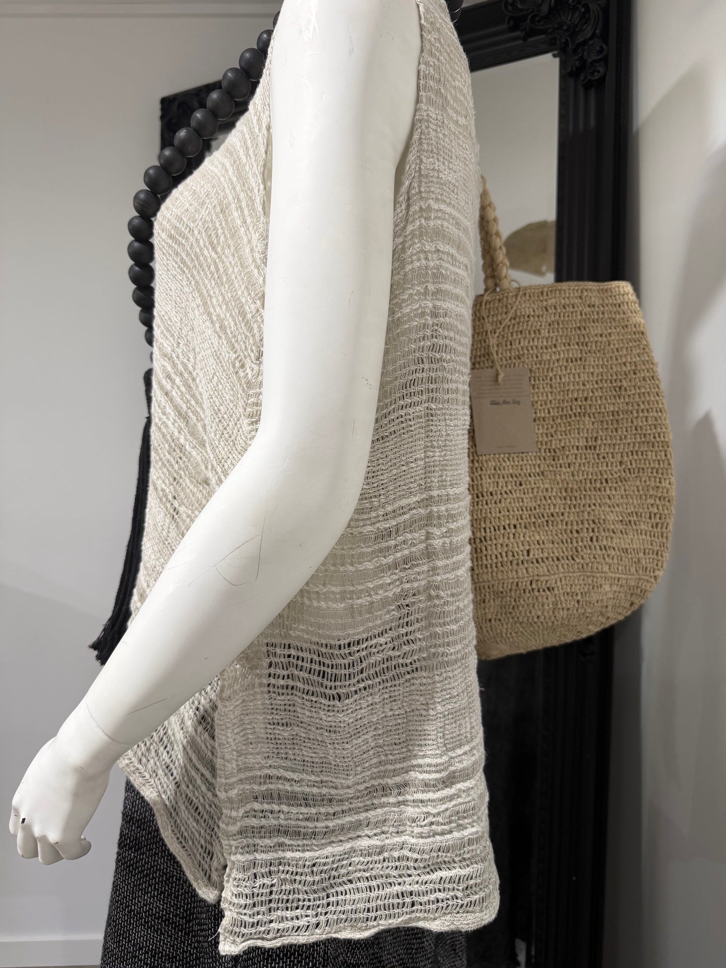 Mannequin wearing a textured beige linen top with a woven bag in the background