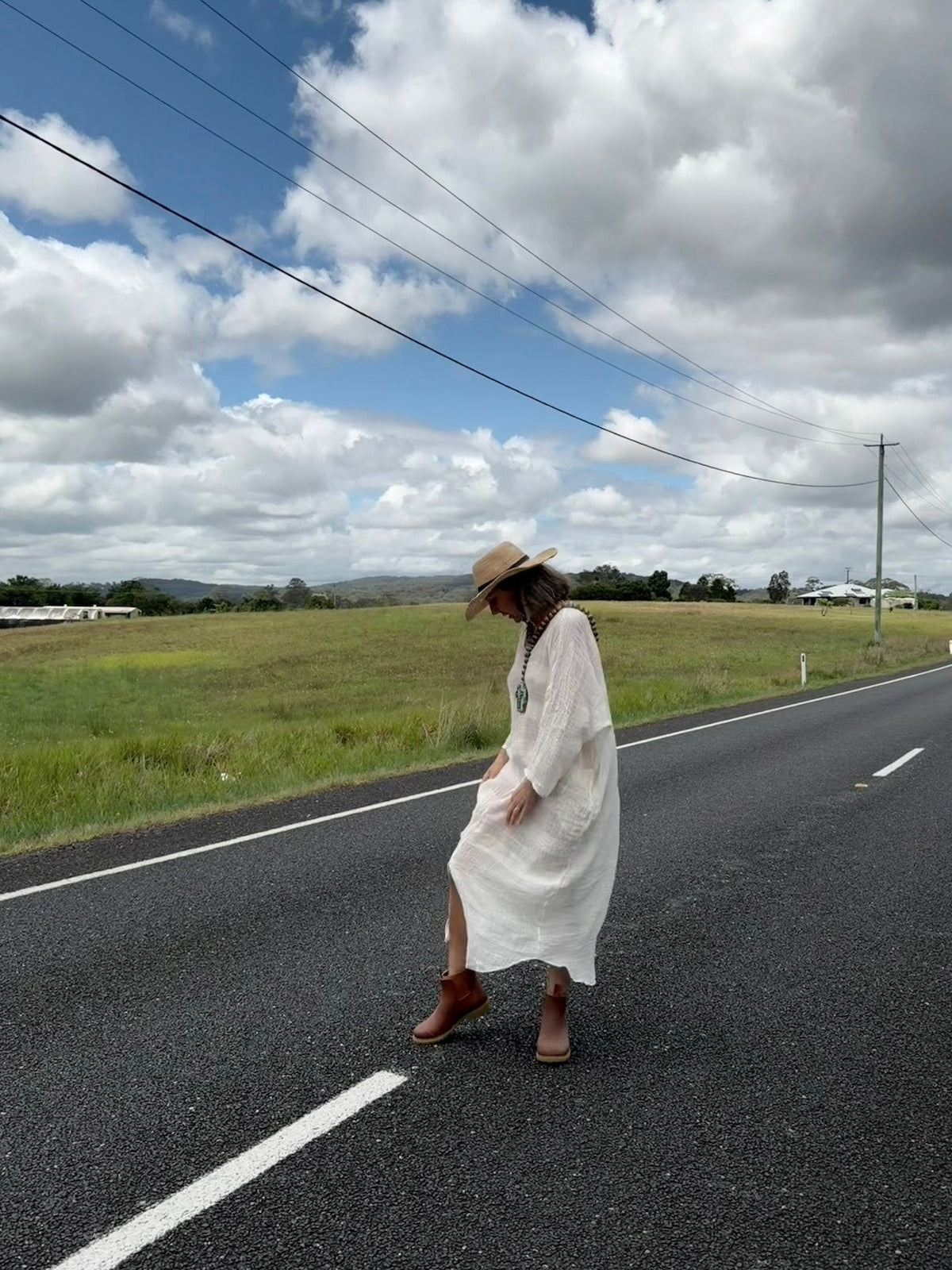 Person in a white linen dress standing on a road with a scenic background