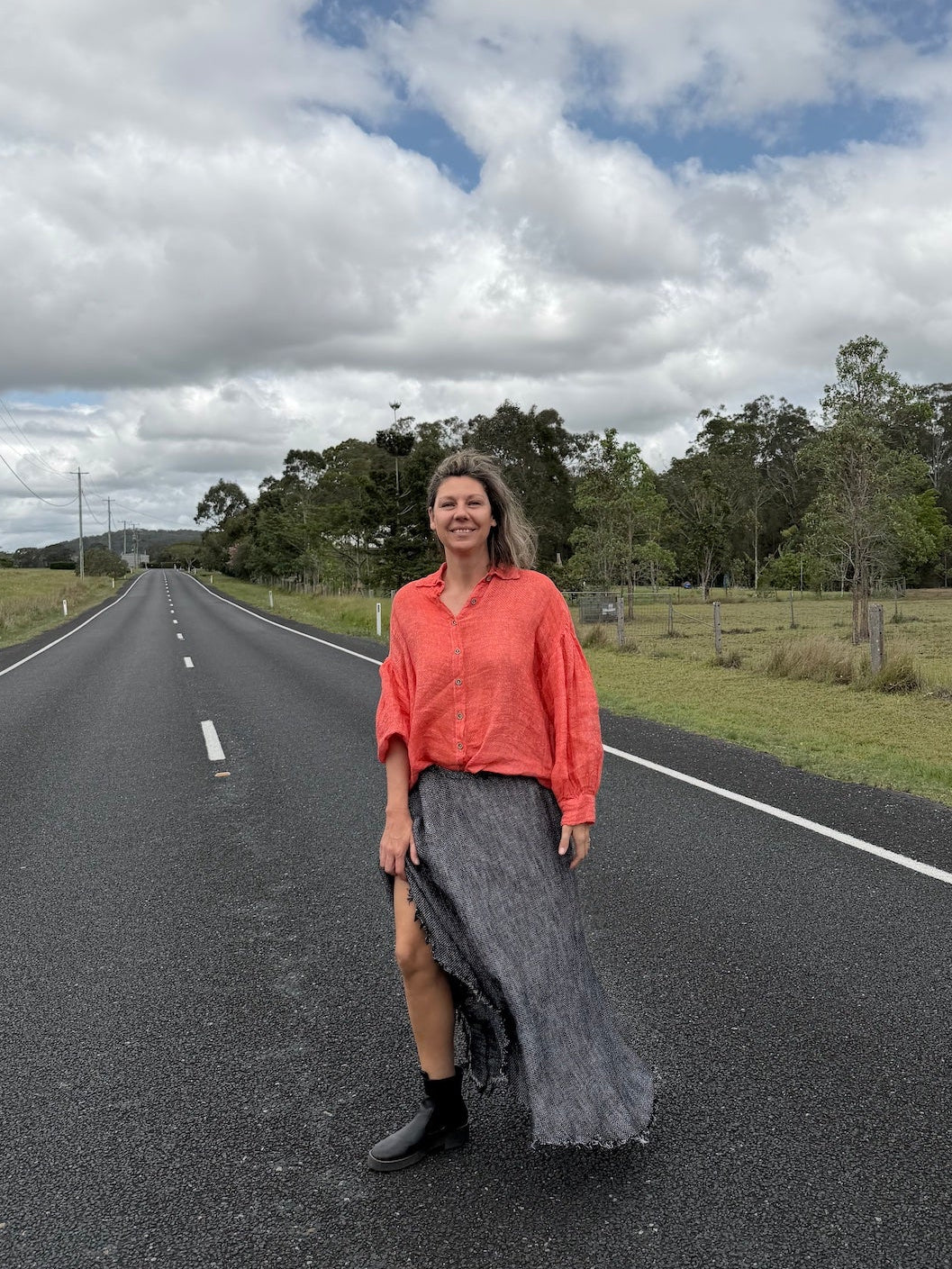 Woman standing on a road wearing estilo emporio with a cloudy sky and trees in the background