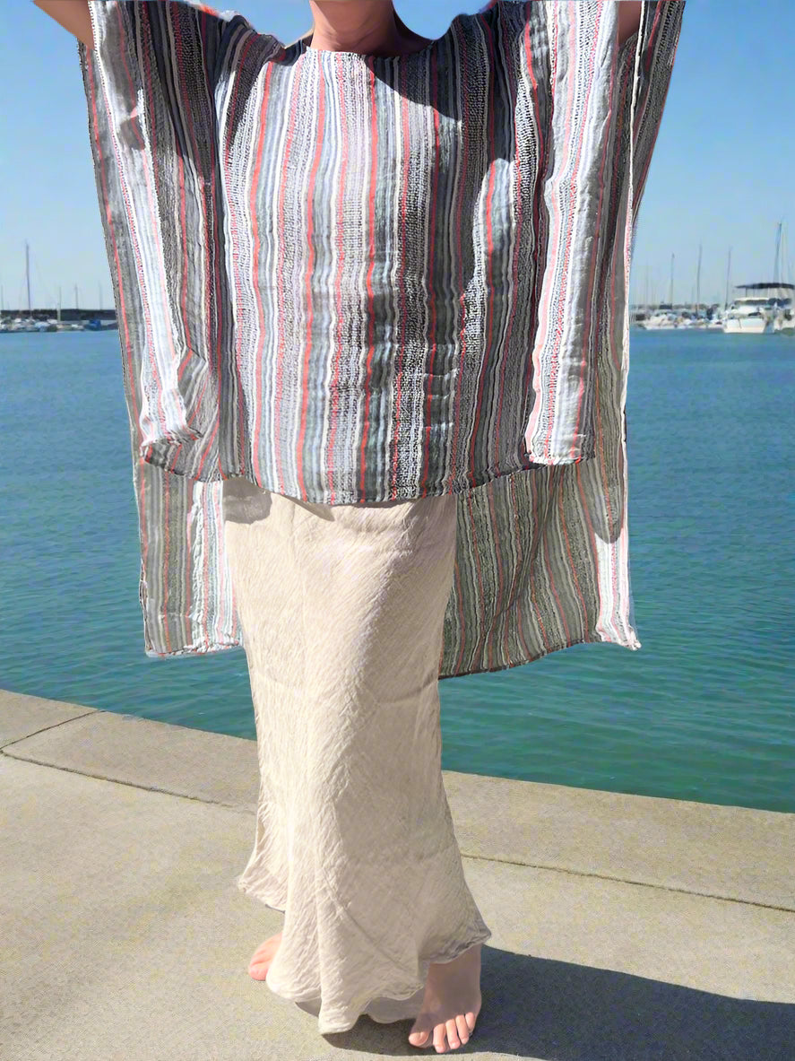 Person wearing a striped shirt and light pants standing on a sidewalk with grass and trees in the background