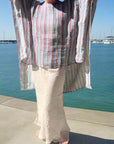Person wearing a striped shirt and light pants standing on a sidewalk with grass and trees in the background