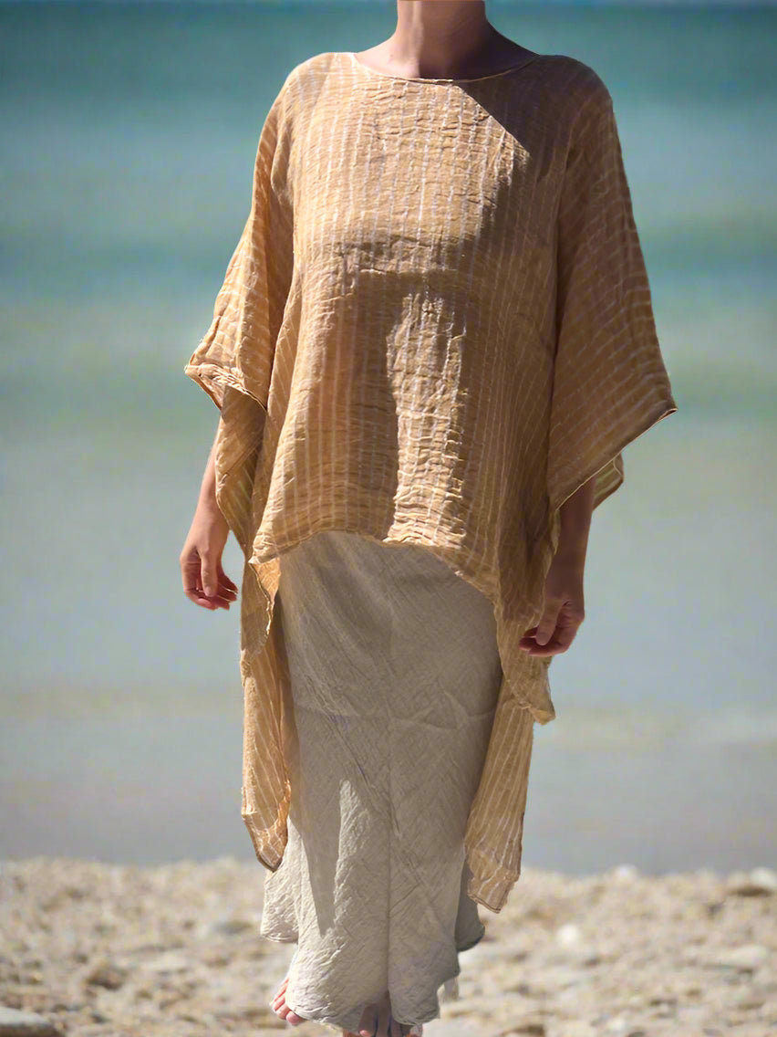 Person wearing a beige dress standing on a concrete surface with grass and trees in the background