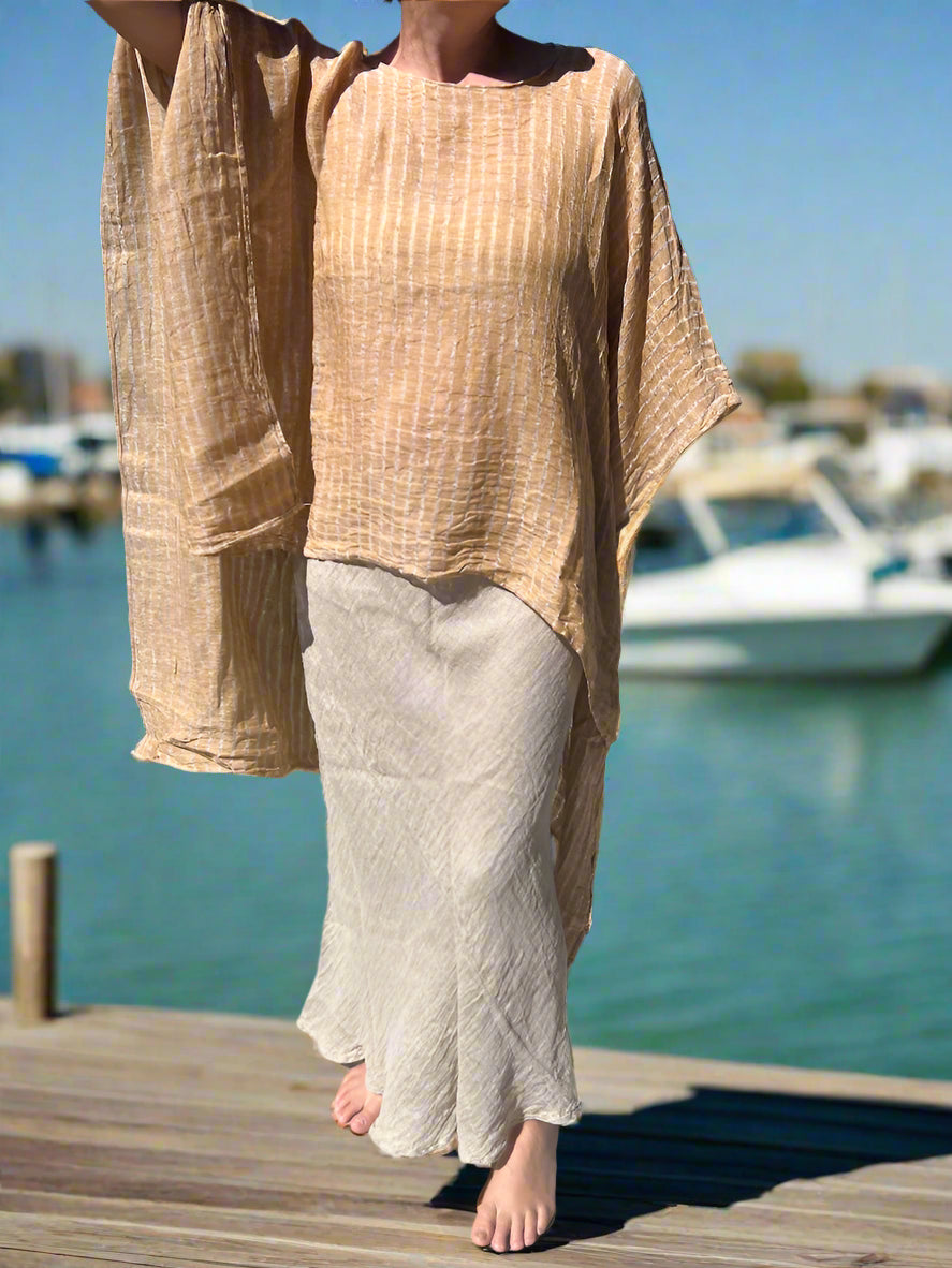 Person wearing a beige outfit standing outdoors on a concrete path with grass and trees in the background.