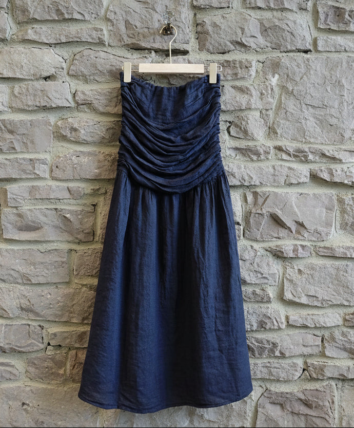 Navy blue strapless dress hanging on a wooden hanger against a light wooden panel background