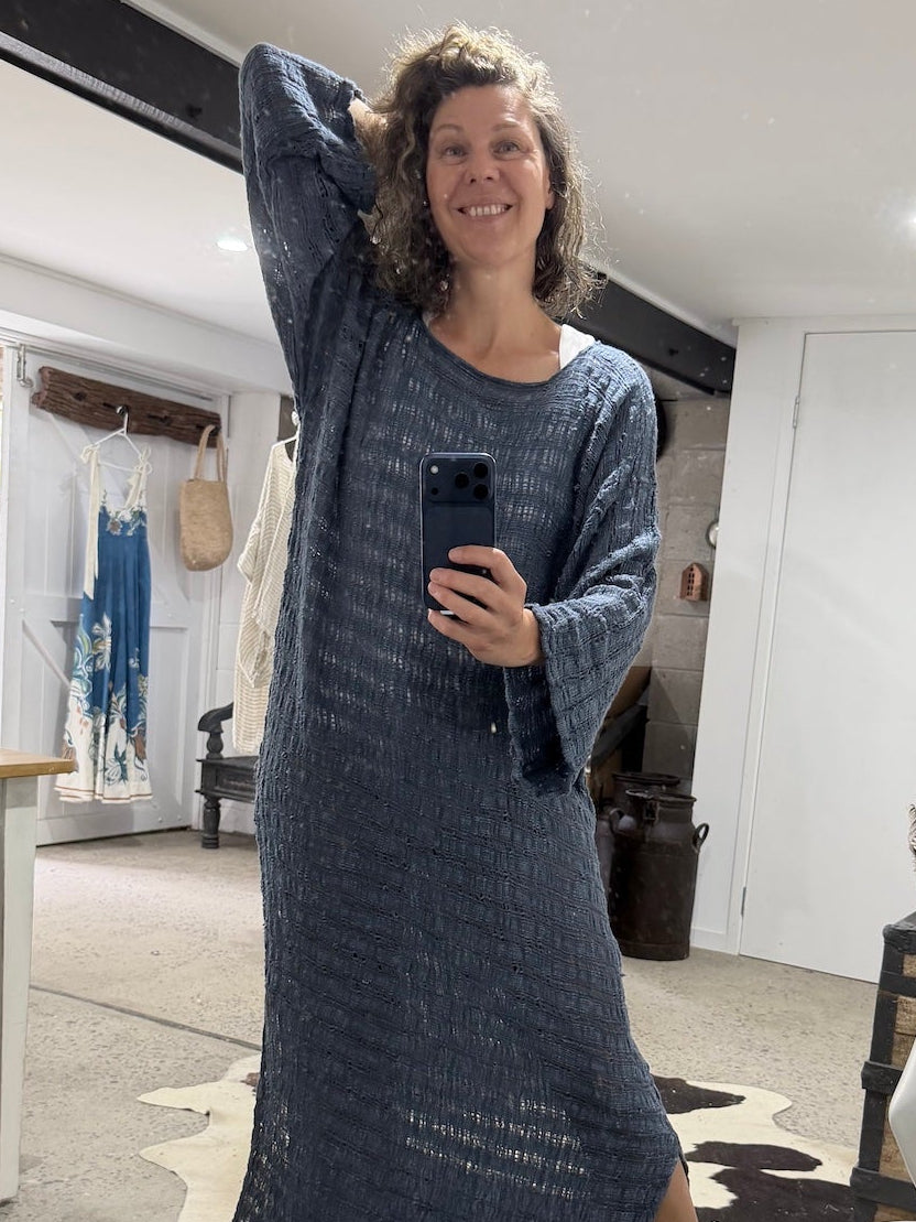 Woman taking a mirror selfie wearing a long blue la bottega di brunella linen dress in a room with a mannequin and furniture.