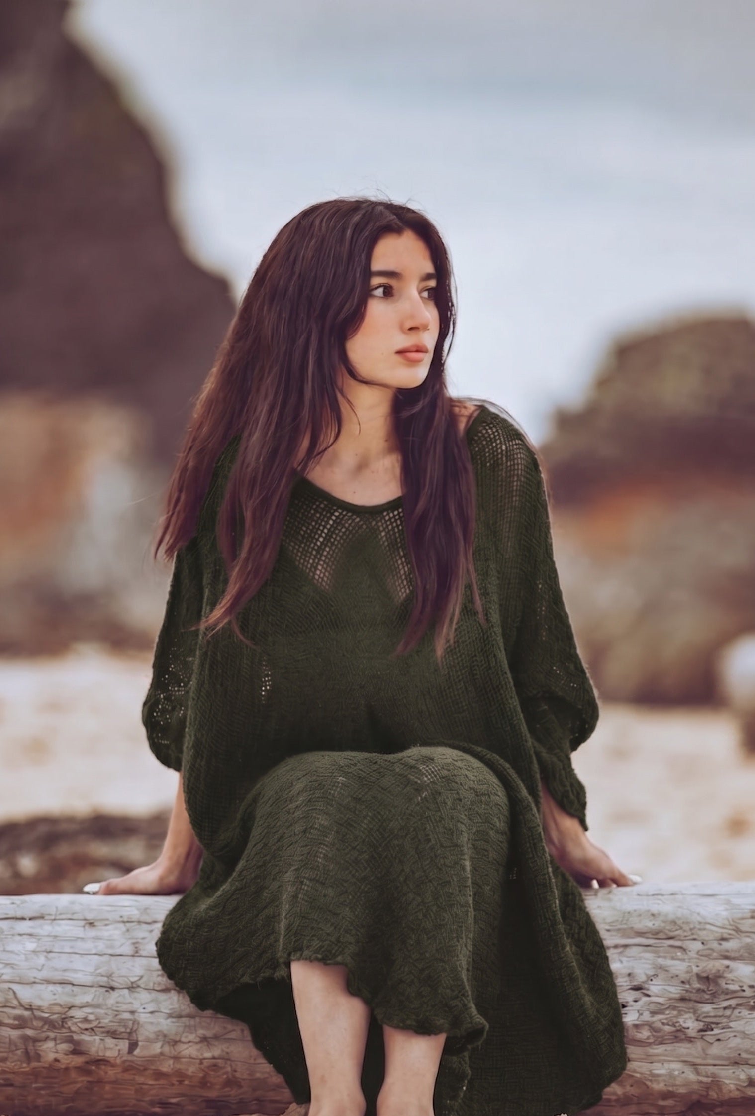 Woman in a green dress sitting on a log by a body of water