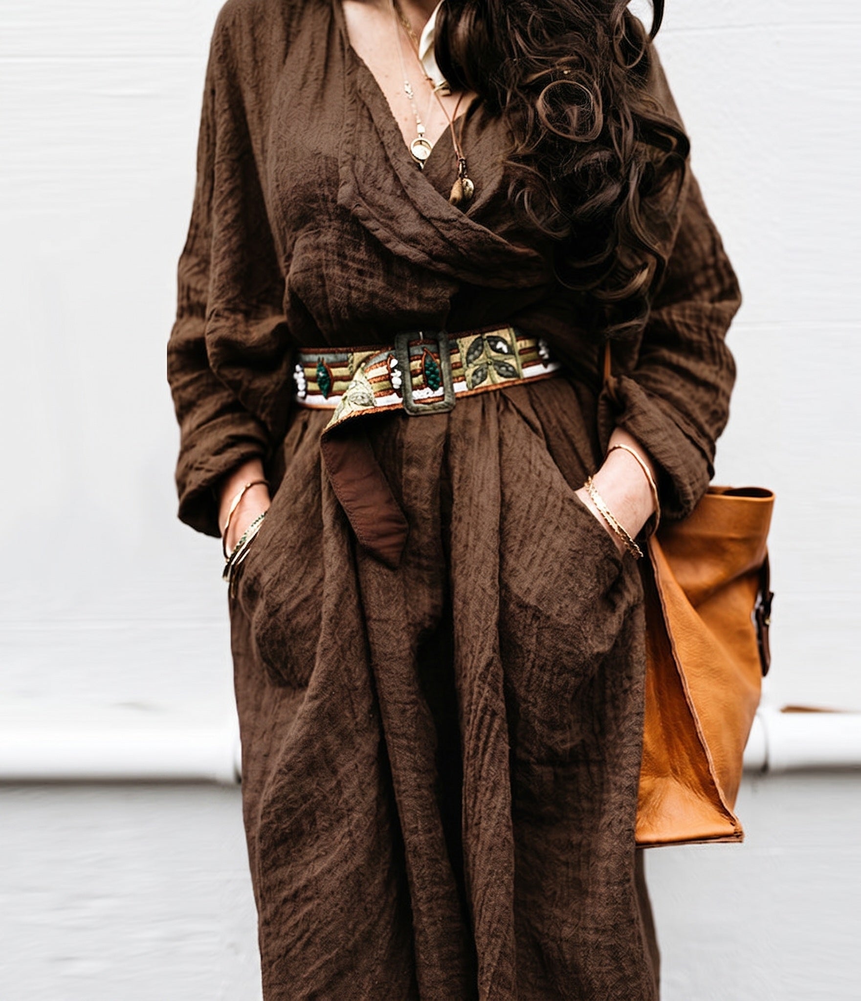 Person wearing a brown outfit with a belt and holding a brown bag against a light background