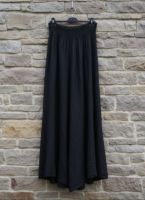 Black skirt hanging on a hanger against a stone wall.
