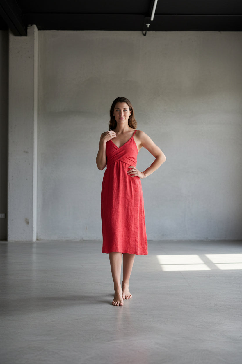 Woman in a red dress standing in a minimalistic room with gray walls and floor.