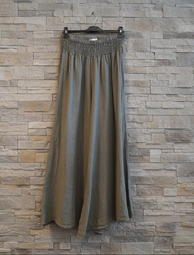 Long green skirt on a hanger against a wooden wall.