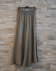 Long green skirt on a hanger against a wooden wall.